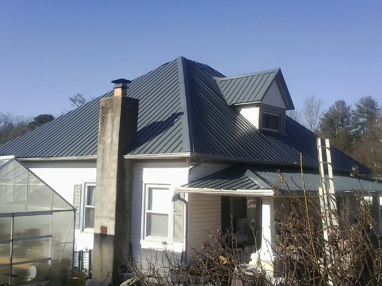 Dark blue standing seam metal roof on a white farmhouse with dormer — Slate & Tile Roof Repair by Roofing Brothers in Oxbow
