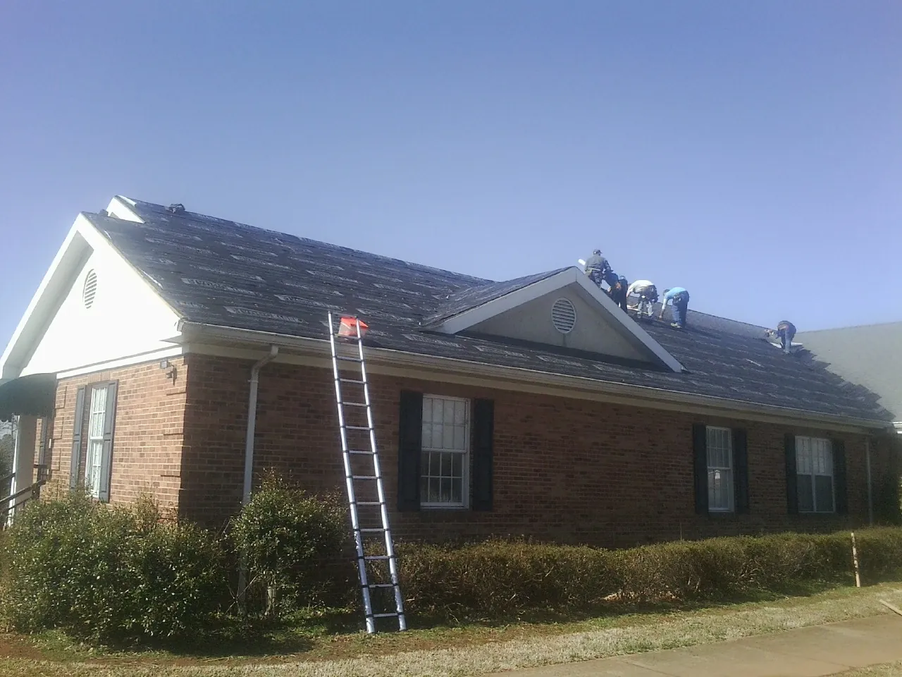 Crew tearing shingles off a brick ranch roof with a ladder set — Emergency Roof Repair work by our crew in Oxbow