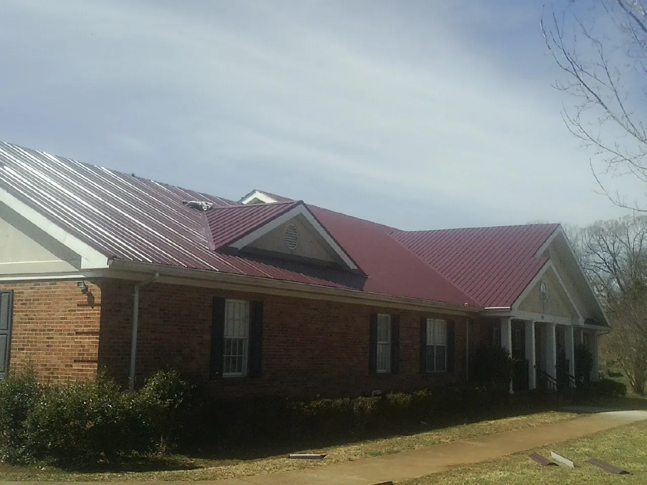 Red metal roof with gabled entries on a long brick building, from a Hail Damage Roof Repair job in Oxbow