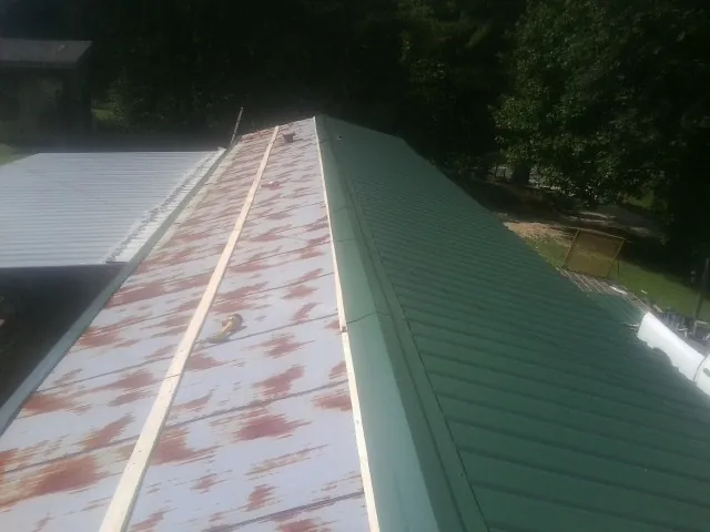 Old rusted panels beside newly installed green metal roofing — Wind Damage Roof Repair by Roofing Brothers in Oxbow
