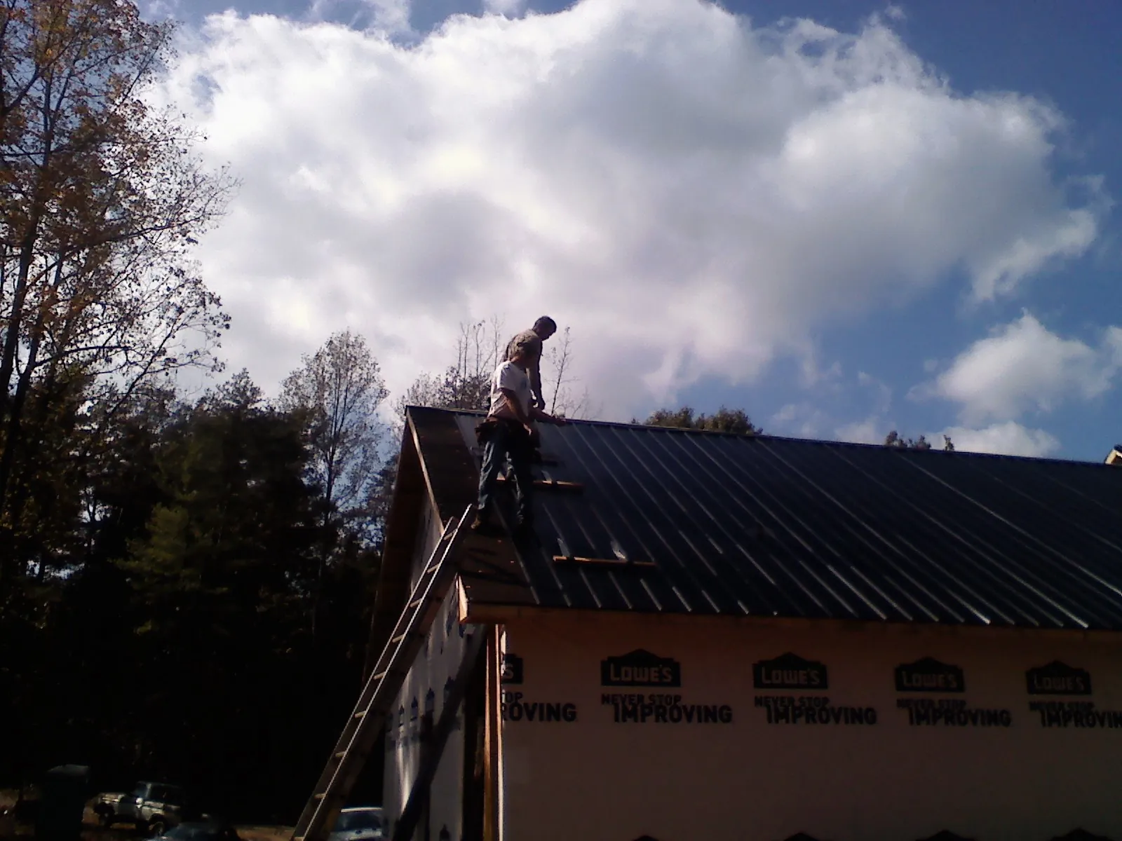 Roofer fastening dark metal panels high against a cloudy sky, from a Roof Inspection job in Oxbow