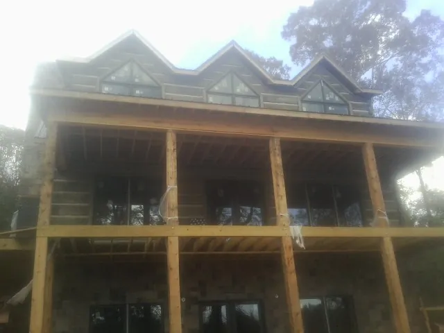 Dormers and porch framing on a large log home under construction — Roof Coating work by our crew in Oxbow