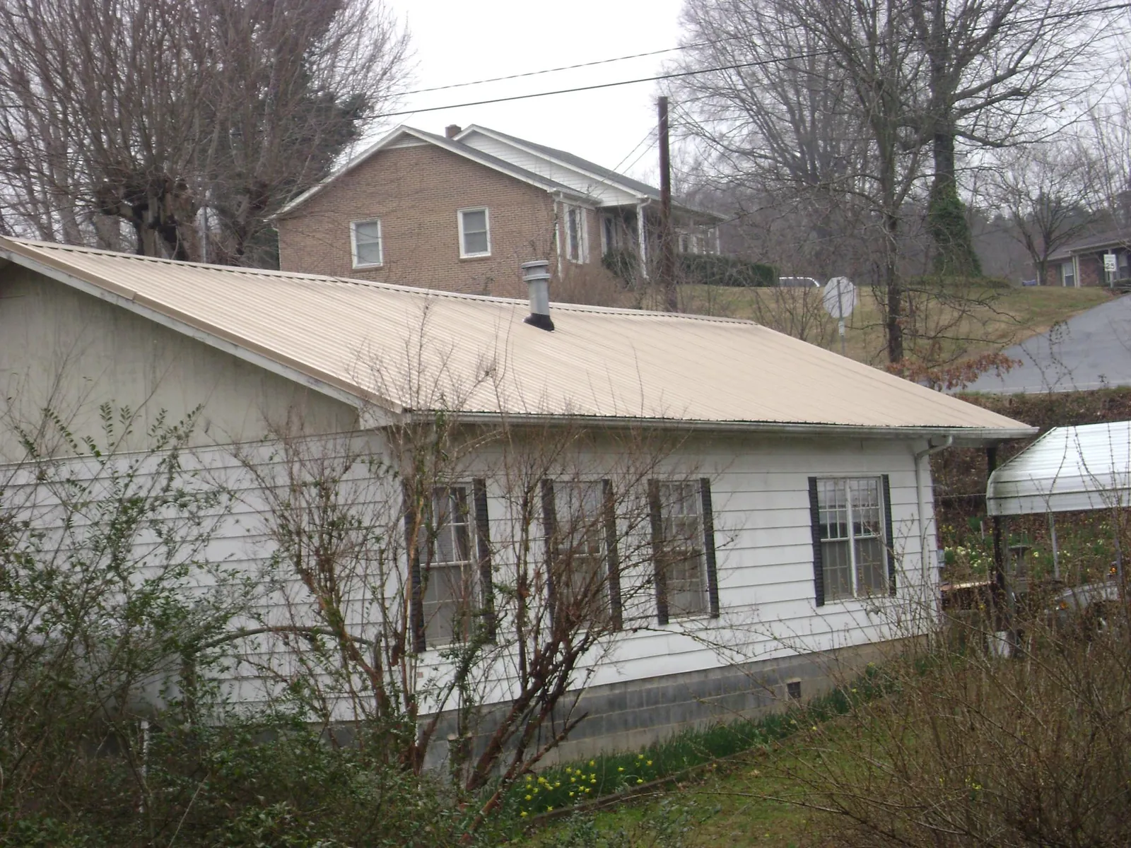 Tan metal roof on a white sided house set into a hillside — Commercial Roofing by Roofing Brothers in Oxbow