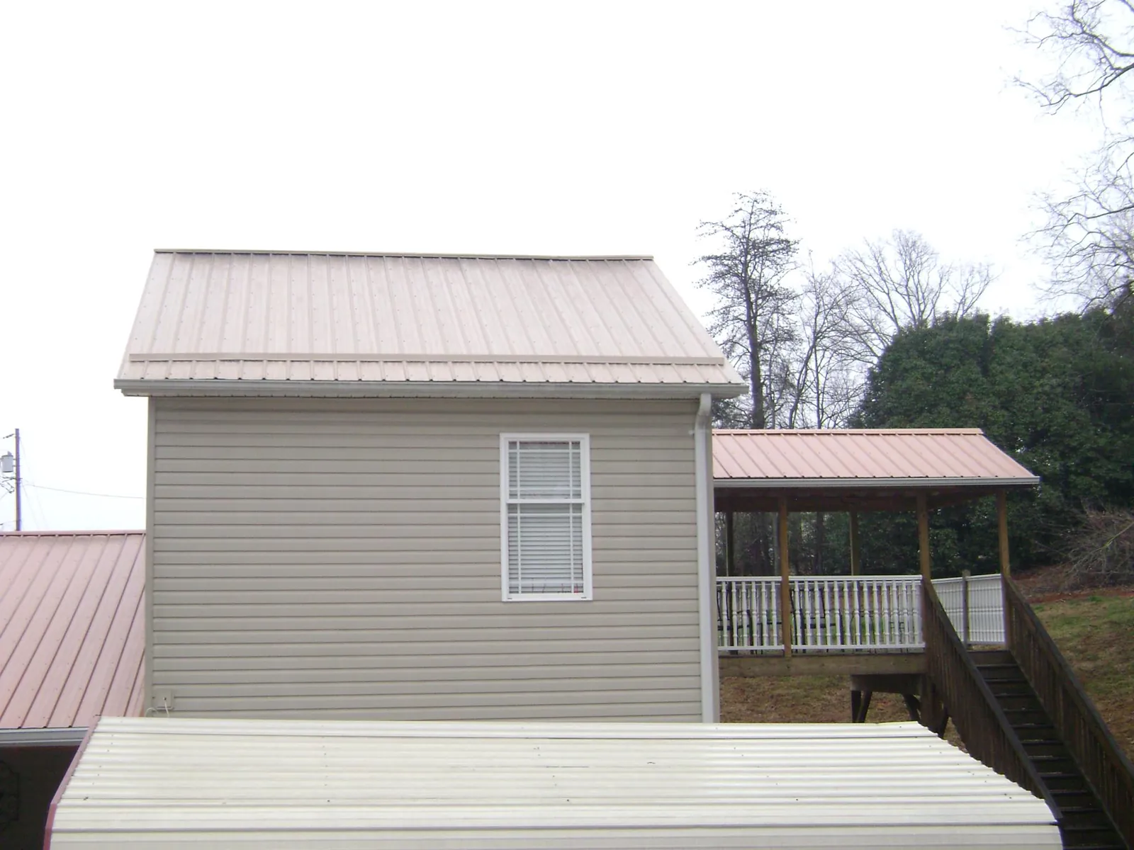 Tan metal roofs on a two story addition and attached porch, from a Roof Replacement job in Oxbow